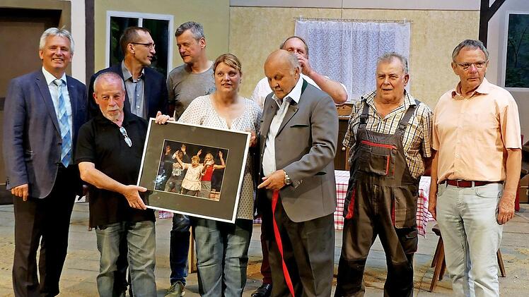 Vor dem Bühnenbild von "Widder Dahaam" präsentiert Martin Ritter (Zweiter von links) auf der Bühne eines seiner Szenenfotos der diesjährigen Theaterstücke. Mit dabei (von rechts) Vorsitzender Siegfried Küspert, Dieter Krause, Walter Richter, Werner Eberhardt (verdeckt), Silke Neukam-Ködel, Mathias Ebert, Gerd Kammerer, Bürgermeister Werner Diersch. Foto: Dieter Hübner