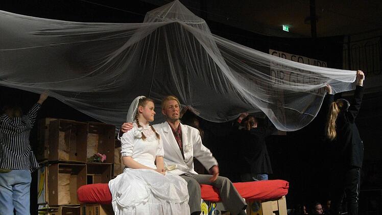 Polly Peachum (Camille Zenses) im Liebeswahn: Sie hat Macheath alias Mackie Messer (Winona Giese) geheiratet und sitzt nun mit ihm auf dem Ehebett.  Foto: Joachim Rübel