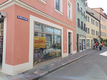 Ein neues Outdoor-Gesch&auml;ft er&ouml;ffnet im Sommer in der Ke&szlig;lerstra&szlig;e, Bamberg, in einem rosa Geb&auml;ude. Schaufensterwerbung ist sichtbar. Passanten sind auf der ruhigen Stra&szlig;e unterwegs.