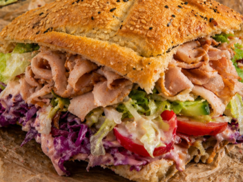 Ein D&ouml;nersandwich mit knusprigem Sesambrot, gef&uuml;llt mit Fleisch, Rotkohl, Salat und Tomaten, angerichtet auf Papier. Es ist die fr&auml;nkische Version eines D&ouml;ner-Imbiss-Klassikers.