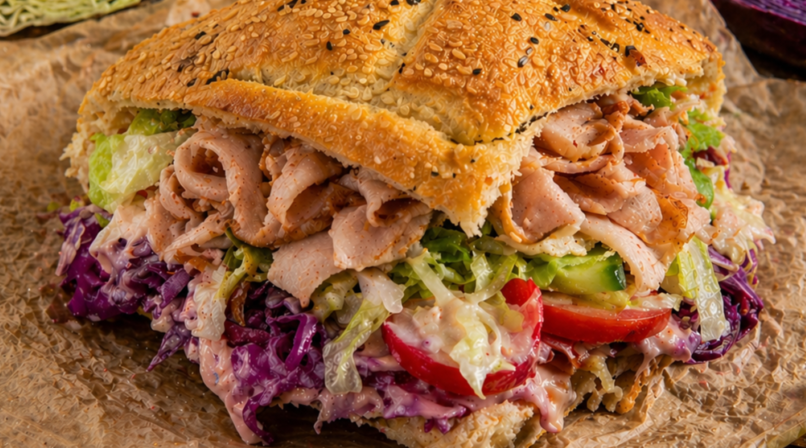 Ein D&ouml;nersandwich mit knusprigem Sesambrot, gef&uuml;llt mit Fleisch, Rotkohl, Salat und Tomaten, angerichtet auf Papier. Es ist die fr&auml;nkische Version eines D&ouml;ner-Imbiss-Klassikers.