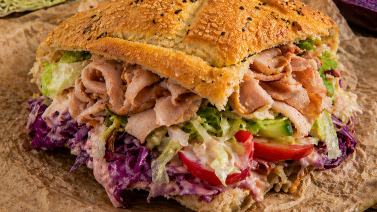 Ein D&ouml;nersandwich mit knusprigem Sesambrot, gef&uuml;llt mit Fleisch, Rotkohl, Salat und Tomaten, angerichtet auf Papier. Es ist die fr&auml;nkische Version eines D&ouml;ner-Imbiss-Klassikers.