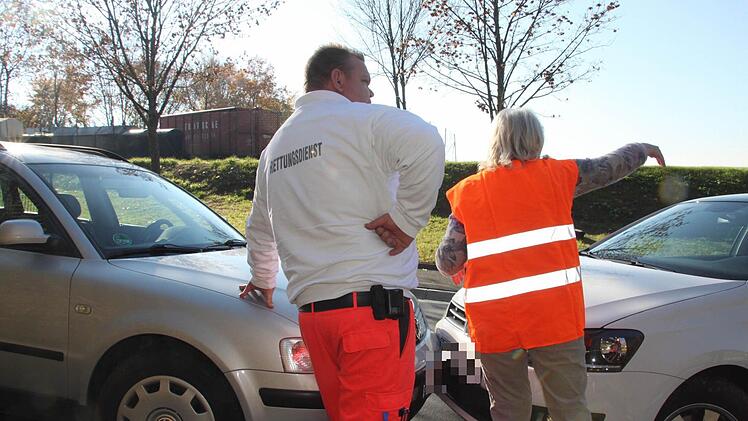 Die von oben kommende Autofahrerin (mit Warnweste) schildert dem Rettungssanitäter, wie das entgegenkommende Fahrzeug erst auf die Böschung des Wertstoffhofes (im Hintergrund) schleuderte und dann zurück auf die Gegenfahrbahn rollte.  Foto: Andreas Oswald