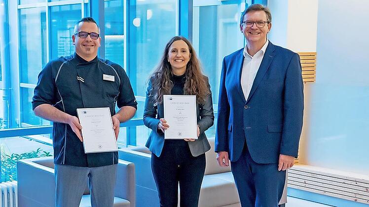 Feiern am Standort Bad Bocklet 25-j&auml;hriges Dienstjubil&auml;um (v.l.): Sebastian Gr&ouml;schl, K&uuml;chenchef der Hescuro Klinik Bad Bocklet, und Kaufm&auml;nnische Leiterin Dr. Antje Geier (jeweils mit Ehrenurkunde der IHK W&uuml;rzburg-Schweinfurt). Es gratuliert Steph...