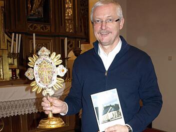 Franz Behrschmidt, Erster Vorsitzender des Heimatgeschichtlichen Arbeitskreises Wallenfels, zeigt den neuen Kirchenführer und die Reliquienmonstranz vom Kreuz Christi. Foto: Susanne Deuerling