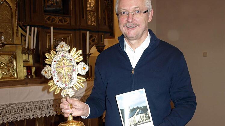 Franz Behrschmidt, Erster Vorsitzender des Heimatgeschichtlichen Arbeitskreises Wallenfels, zeigt den neuen Kirchenführer und die Reliquienmonstranz vom Kreuz Christi. Foto: Susanne Deuerling