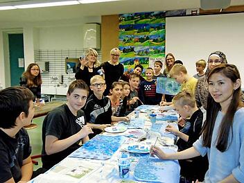 Sarah (r.) liebt Kunst und sie war der Grund, dass die siebte Klasse des M-Zuges und die Integrationskünstler an der Wanderausstellung nach Minsk teilnehmen. Begeistert versuchen sie, Claude Monets Seerosen ebenso ausdrucksstark auf das Zeichenpapier zu bringen. Die Künstlerin Berit Klasing (hinten links, hält die bemalte Hand hoch) gibt Tipps und ist begeistert von den Werken. Foto: Petra Malbrich