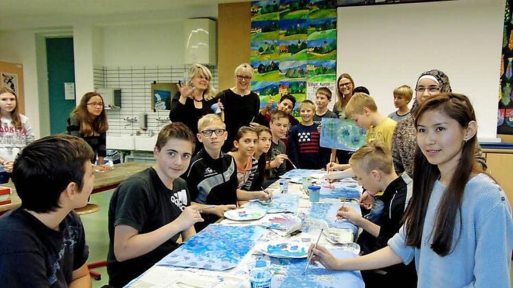 Sarah (r.) liebt Kunst und sie war der Grund, dass die siebte Klasse des M-Zuges und die Integrationskünstler an der Wanderausstellung nach Minsk teilnehmen. Begeistert versuchen sie, Claude Monets Seerosen ebenso ausdrucksstark auf das Zeichenpapier zu bringen. Die Künstlerin Berit Klasing (hinten links, hält die bemalte Hand hoch) gibt Tipps und ist begeistert von den Werken. Foto: Petra Malbrich