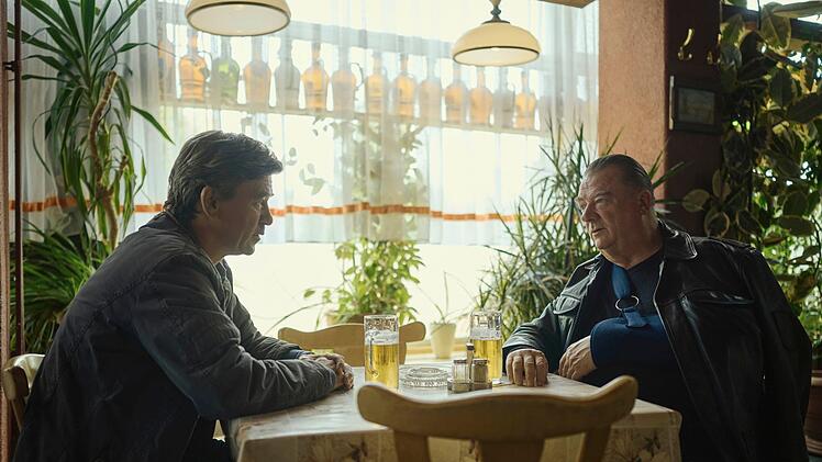 Michael Lehmann (Peter Schneider) und Henry Koitzsch (Peter Kurth) diskutieren Leben und Fall in einer Kneipe, in der die DDR nie untergegangen zu sein scheint.