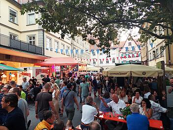 Straßenfest mit vielen Menschen in Bamberg: Bunte Wimpel schmücken die Szene, Essenstände und Bierzelte sind gut besetzt. Eine lebendige Atmosphäre unter grünen Bäumen.