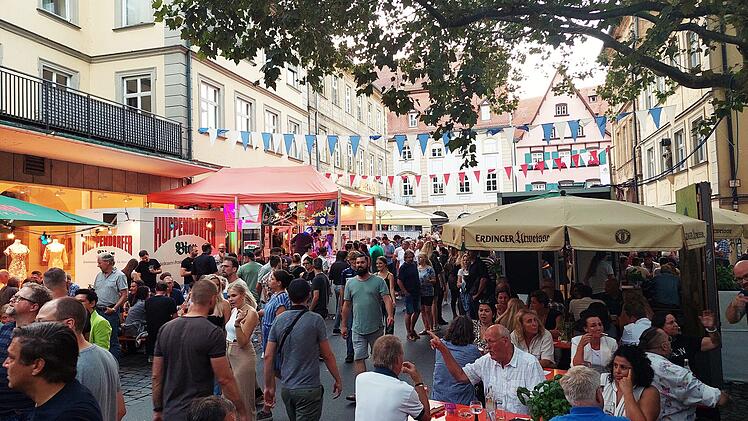 Straßenfest mit vielen Menschen in Bamberg: Bunte Wimpel schmücken die Szene, Essenstände und Bierzelte sind gut besetzt. Eine lebendige Atmosphäre unter grünen Bäumen.