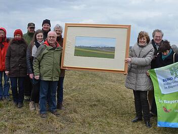 Mitglieder des Bundes Naturschutz und Gegner des neuen Flugplatzes fokussieren mit einem Bilderrahmen den Blick auf das Gelände, auf dem der neue Landeplatz gebaut werden soll. Foto: Rainer Lutz