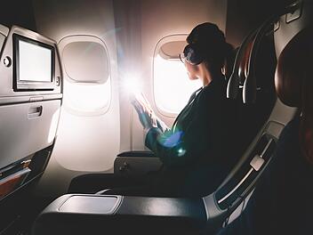 Female tourist in headphones listening audio book and looking in airplane window enjoying flight. Young 25 years old woman with cellular phone in hands sitting on seat during flight in first class Weibliche Touristin mit Kopfh&ouml;rern h&ouml;rt ein H&ouml;rbuch und schaut aus dem Flugzeugfenster, um den Flug zu genie&szlig;en. Junge 25-j&auml;hrige Frau mit Handy in der Hand sitzt w&auml;hrend des Fluges in der First Class auf ihrem Sitzplatz.