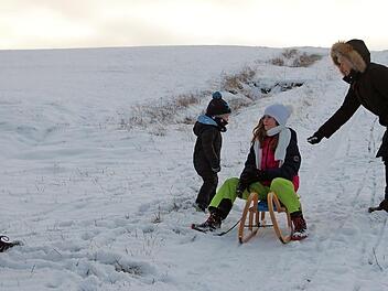 Die Kinder Lina und Sören haben viel Spaß beim Schlittenfahren. Die Erwachsenen leisten Hilfestellung und sorgen für den nötigen Schwung, wenn es auf dem Schnee dahingeht.