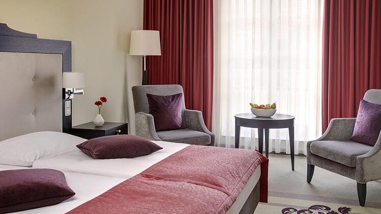 Elegantes Hotelzimmer in Bamberg mit Doppelbett, roten Akzenten, Sitzbereich und Fruchtschale. Gemütliches Ambiente mit stilvoller Einrichtung. Ideal für einen komfortablen Aufenthalt.