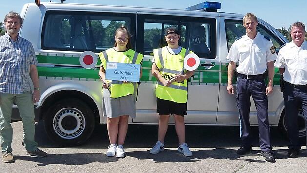 Die beiden Verkehrserzieher der Polizeiinspektion Ha&szlig;furt , Dominique Heim (rechts) und Matthias Krapf (Zweiter von rechts), &uuml;berreichten den beiden Sch&uuml;lerlotsen der Waldorfschule, Lorena Hertinger und Jakob Zehendner, stellvertretend f&uuml;r alle anderen freiwillig Engagierten im Landkreis die von der Kreisverkehrswacht Ha&szlig;berge gesponsorten Warengutscheine; links Lehrer Walter-Johannes Pirling. Foto: Christian Licha
