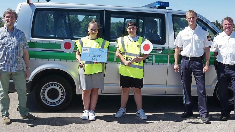 Die beiden Verkehrserzieher der Polizeiinspektion Ha&szlig;furt , Dominique Heim (rechts) und Matthias Krapf (Zweiter von rechts), &uuml;berreichten den beiden Sch&uuml;lerlotsen der Waldorfschule, Lorena Hertinger und Jakob Zehendner, stellvertretend f&uuml;r alle anderen freiwillig Engagierten im Landkreis die von der Kreisverkehrswacht Ha&szlig;berge gesponsorten Warengutscheine; links Lehrer Walter-Johannes Pirling. Foto: Christian Licha