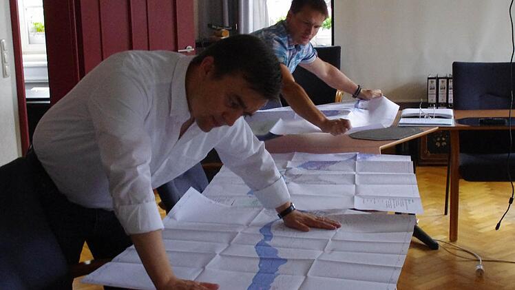 Bürgermeister Jens Korn (links) und Frank Jakob von der Stadtverwaltung reihen die Pläne für die Stadt Wallenfels auf. Das obere Bild zeigt einen Ausschnitt mit den Flächen (blau), auf die sich ein hundertjähriges Hochwasser den Berechnungen nach auswirken würde. Foto: Marco Meißner