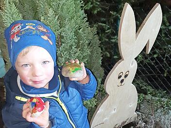 Der dreijährige Felix zeigt stolz seine handbemalten Steine, die er neben dem Osterhasen im Garten ablegt.