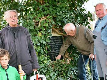 Gerhard Wulz, Werner Eberth und Gerd Schindelmann (von links) kümmern sich mit einigen Helfern um den denkmalgeschützen Kapellenfriedhof. Die Grabmäler sollen nicht durch wuchernde Pflanzen beschädigt werden. Bei diesem Grab ist das Grabmal allerdings zum Naturdenkmal geworden.  Foto: Werner Vogel