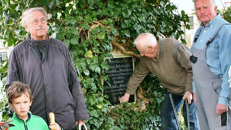 Gerhard Wulz, Werner Eberth und Gerd Schindelmann (von links) kümmern sich mit einigen Helfern um den denkmalgeschützen Kapellenfriedhof. Die Grabmäler sollen nicht durch wuchernde Pflanzen beschädigt werden. Bei diesem Grab ist das Grabmal allerdings zum Naturdenkmal geworden.  Foto: Werner Vogel