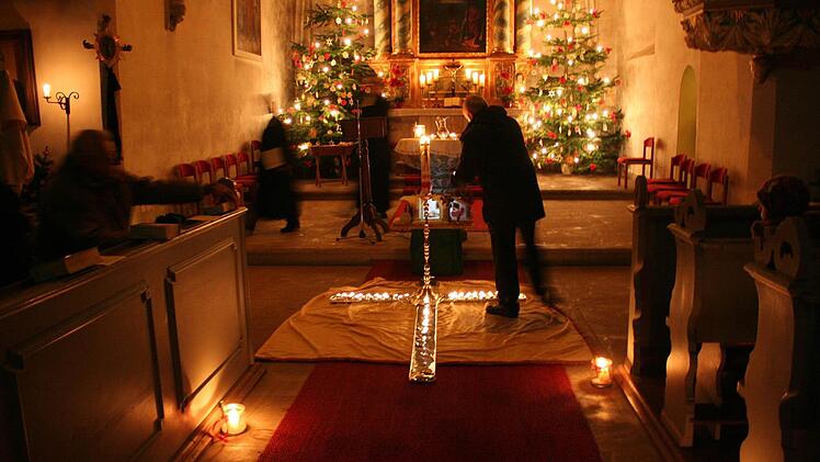 Gemeindemitglieder zünden in dem nur von Kerzen erleuchteten Gotteshaus Lichter an und stellen sie auf ein ausgelegtes Kreuz,.  Foto: Evi Seeger