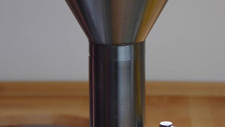 Die Samen oder Nüsse werden der Ölpresse über einen Trichter zugeführt.