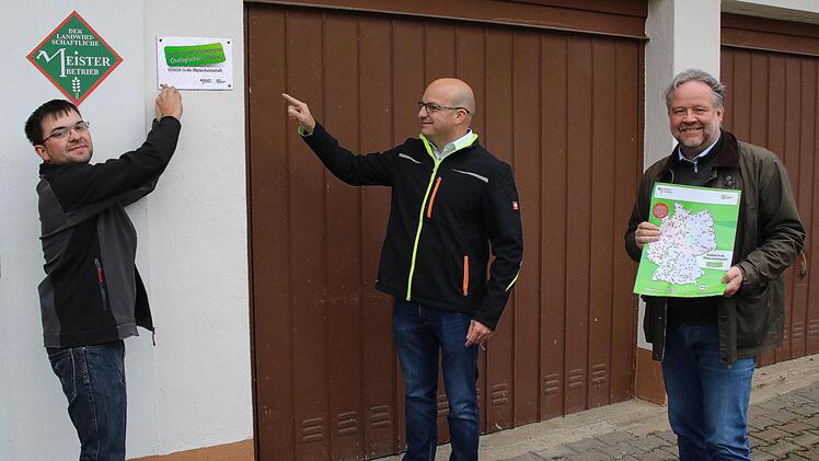 "Demonstrationsbetrieb ökologischer Landbau" ist nun der  Landwirtschaftsbetrieb von Andreas Schlembach (links) in Kleinwenkheim.  Bürgermeister Michael Kastl (Mitte) freut sich mit ihm. Aus Bonn war Thomas  Kollritsch (rechts) von der Koordinationsstelle Demonstrationsbetriebe  ökologischer Landbau gekommen, um das Hinweisschild am Hofladen zu  überbringen. Foto: Dieter Britz