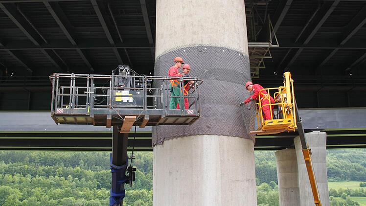 Bauarbeiter umwickeln die Stellen, wo der Pfeiler kippen soll, mit Maschendrahtzaun.