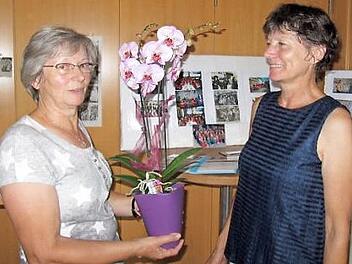 Gründungsmitglied Claudia Gunzelmann (links) mit einem Blumenpräsent für Rosi Labisch. Im Hintergrund ist eine Ausstellung von Fotos und Zeitungsberichten der letzten 50 Jahre zu sehen. Foto: Monika Schütz