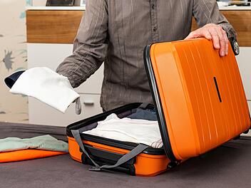 A man folds things in an orange-colored travel suitcase on wheels. Travel preparation.Ein Mann faltet Dinge in einem orangefarbenen Reisekoffer auf Rädern. Reisevorbereitung.