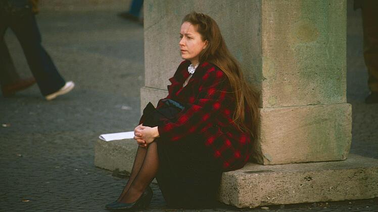 Eine Frau sitzt auf einem Stück der Berliner Mauer.