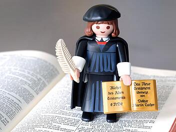 Playmobil-Lutherfigur mit Feder und Bibel auf einer Lutherbibel epd