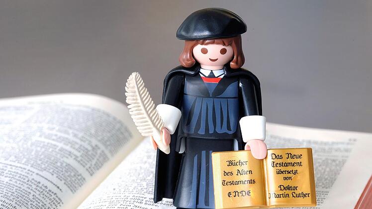 Playmobil-Lutherfigur mit Feder und Bibel auf einer Lutherbibel epd