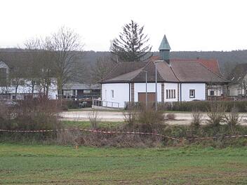 Der Friedhofsparkplatz mit den Spuren der aktuellen Vermessung, im Hintergrund das renovierte Leichenhaus. Nach einer Ortseinsicht am Friedhofsparkplatz beschloss der Gemeinderat, den dort vorhandenen Grenz&uuml;berbau eines Nachbargrundst&uuml;cks zu entfernen. Bei diesem R&uuml;ckbau sei die Entw&auml;sserung an der n&ouml;rdlichen Grenze festzulegen. Adelheid Waschka