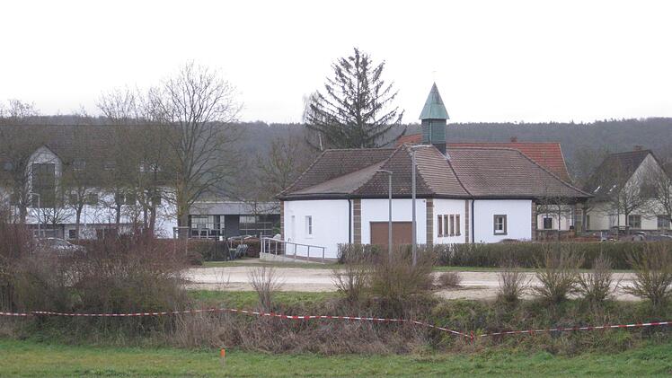 Der Friedhofsparkplatz mit den Spuren der aktuellen Vermessung, im Hintergrund das renovierte Leichenhaus. Nach einer Ortseinsicht am Friedhofsparkplatz beschloss der Gemeinderat, den dort vorhandenen Grenz&uuml;berbau eines Nachbargrundst&uuml;cks zu entfernen. Bei diesem R&uuml;ckbau sei die Entw&auml;sserung an der n&ouml;rdlichen Grenze festzulegen. Adelheid Waschka