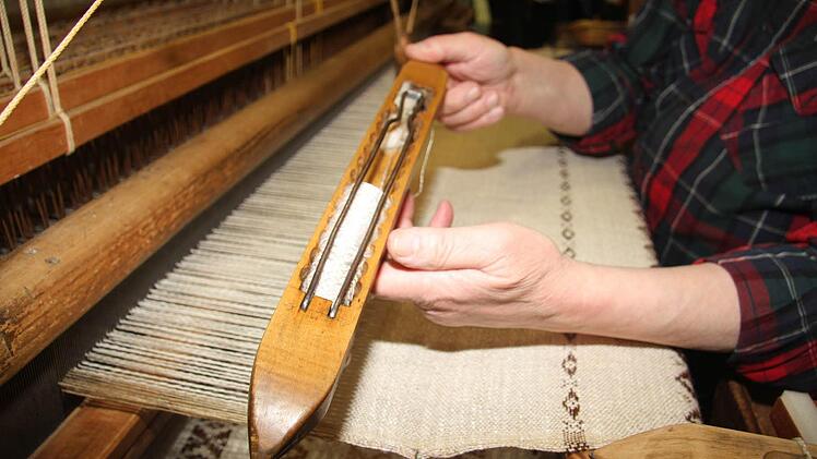 Das Schiffchen wird mit dem Seilzug hin und herbewegt, mit den Füßen bewegt Ludwig Beck die Schäfte des Webstuhls - und die sind wichtig für das Muster .