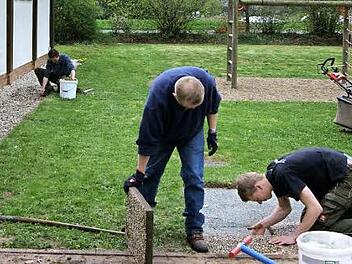 Johannes Fröba (rechts) und Matthias Sprenger pflastern den Untergrund für eine Sitzgruppe. Im Hintergrund sammelt Andreas Fleischmann den Unrat um die Zecherhalle auf. Foto: Hofmann