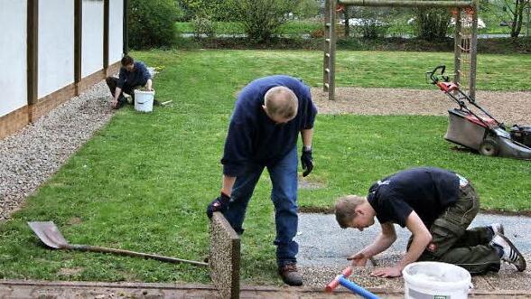 Johannes Fröba (rechts) und Matthias Sprenger pflastern den Untergrund für eine Sitzgruppe. Im Hintergrund sammelt Andreas Fleischmann den Unrat um die Zecherhalle auf. Foto: Hofmann