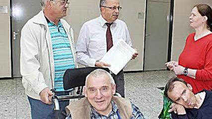 Roland Eyrich (links) und Maria Schüßler überreichten stellvertretendem Landrat Emil Müller ihre Petition zur Einrichtung einer Behinderten-Toilette im Berghaus Rhön. Nutznießer werden auch Robert Nies und Manfred Schüler (im Vordergrund) sein. Foto: Thomas Mäuser