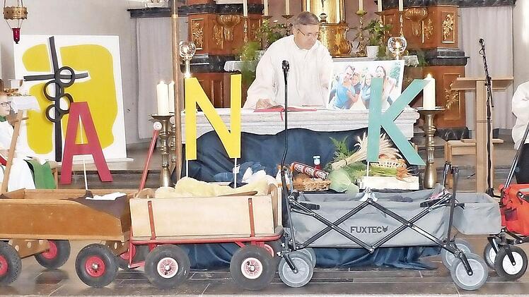 Die Buchstaben an den f&uuml;nf Bollerwagen mit den Erntedankgaben ergeben das Wort Danke. Beim Familiengottesdienst wirkten neben den Kindern, Ministranten und Pfarrer Michael Erhart auch der Diakon Norbert Zettelmeier (Mitte) und der Diakon-Anw&auml;rter Andreas Hofer (rechts) mit.  Foto: Friedbert Bartl