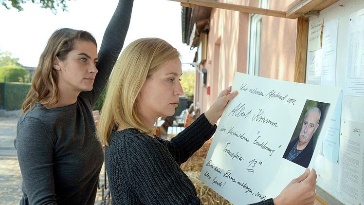 Katrin (Samia Chancrin, links) und Eva (Pina K&uuml;hr) befestigen die Einladung zur Trauerfeier im Aushang. Die Gartenkolonie m&ouml;chte in Ehren an den Ermordeten noch einmal zusammenkommen.