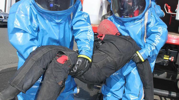 Die Feuerwehrleute bringen in ihren CSA-Anzügen einen verunglückten Mann weg vom Fahrzeug.