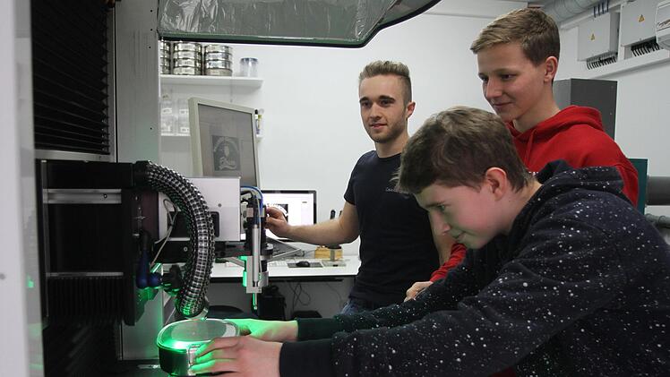 Philipp Muth bei der Arbeit an der Lasermaschine mit Produktionsleiter Simon Schlee (M.) und Wirtschaftspaten Adrian Dümpert (hinten)