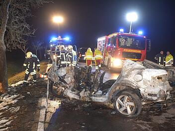 Sachsen-Anhalt, K&ouml;then: Feuerwehrleute und Rettungskr&auml;fte stehen auf einer Landstra&szlig;e hinter einem ausgebrannten Auto. Bei dem Autounfall sind drei Menschen, darunter ein Kind, verbrannt. Ein S&auml;ugling wurde aus dem Wrack gerettet. Foto: Heiko Rebsch/dpa-Zentralbild/dpa