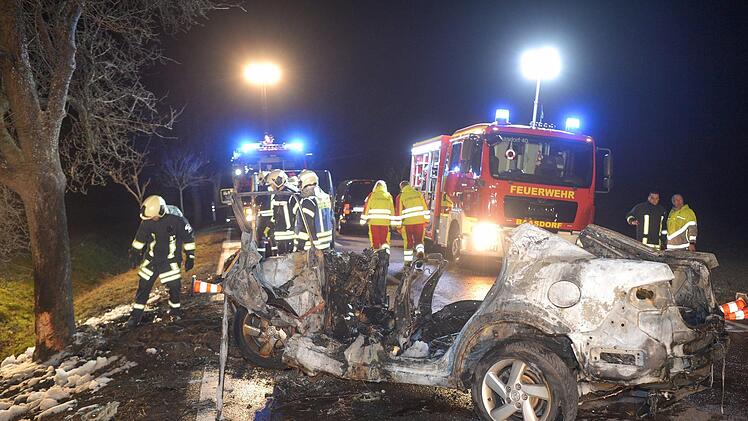 Sachsen-Anhalt, K&ouml;then: Feuerwehrleute und Rettungskr&auml;fte stehen auf einer Landstra&szlig;e hinter einem ausgebrannten Auto. Bei dem Autounfall sind drei Menschen, darunter ein Kind, verbrannt. Ein S&auml;ugling wurde aus dem Wrack gerettet. Foto: Heiko Rebsch/dpa-Zentralbild/dpa