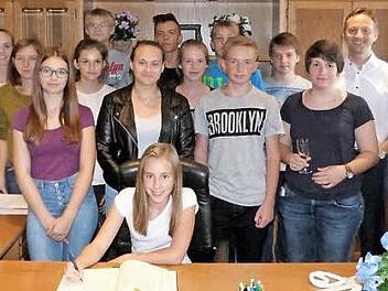 Luisa Sch&ouml;nfeld tr&auml;gt sich in das G&auml;stebuch der Marktgemeinde Mainleus ein. Im Hintergrund die erfolgreichen Tischtennissportler und - sportlerinnen. Foto: Werner Rei&szlig;aus