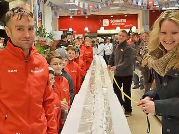 Jörg Kufel und die Fußballjunioren  schauen gespannt zu, wie Monika und Sebastian Hauke  die Länge der Christstollenreihe ermitteln.