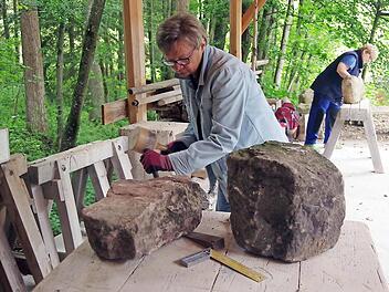 Lore Walker nimmt zum 17. Mal an der Sandsteinwerkstatt teil und fertigt eine Skulptur als Geburtstagsgeschenk. Im Hintergrund arbeitet Antje Mann aus Berlin an einer Skulptur mit dem Motiv einer liegenden Katze, die sie im vergangenen Jahr angefangen hatte.  Foto: Heike Schülein
