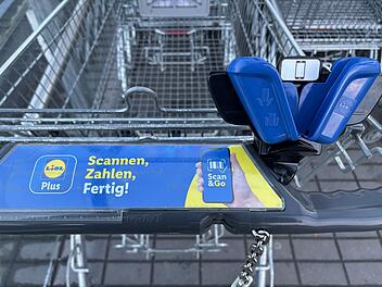 Ein Einkaufswagen mit einem "Scan & Go"-System von Lidl. Es zeigt eine Halterung und Werbung, die schnelles Einkaufen durch Scannen und Bezahlen per App erm&ouml;glicht.
